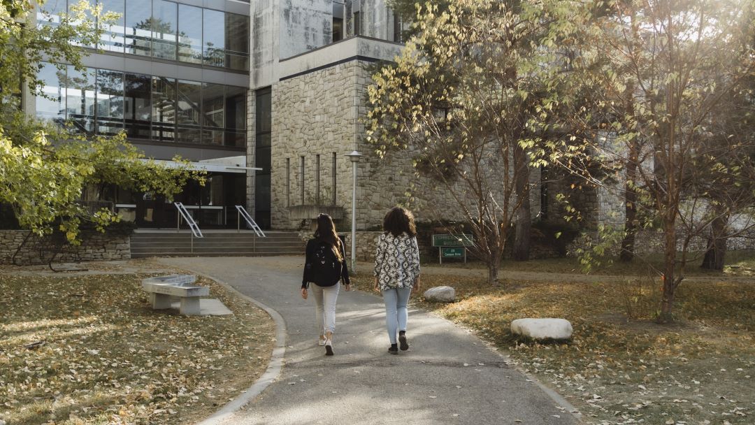 Photo of two young women walking toward the Law Building on the USask campus on a fall day. 